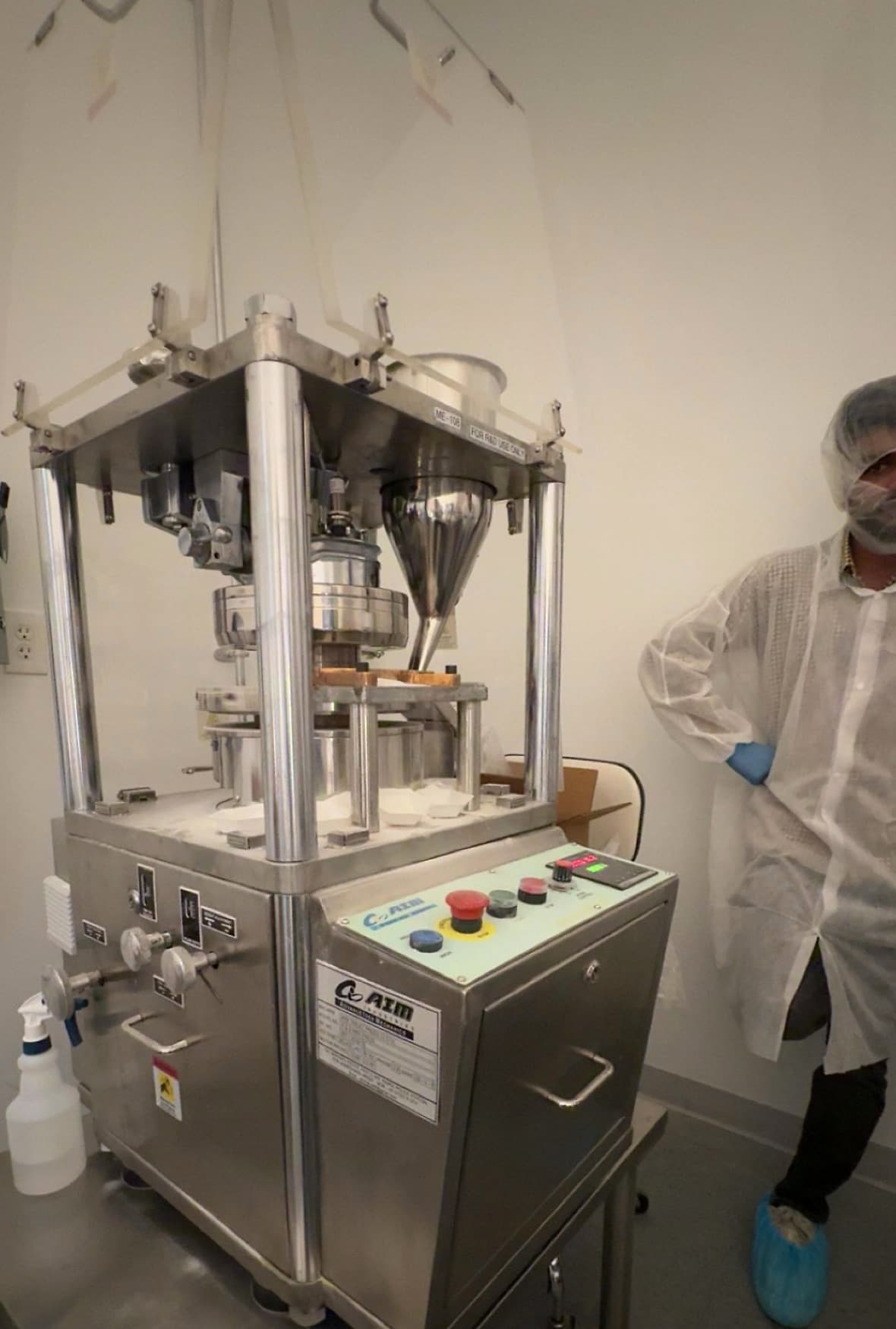 Ananay standing next to a rotary tablet press on the Aavis Pharmaceuticals production floor